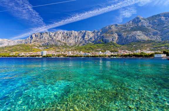 People swimmin in crystal-clear water in Croatia with rocky mountain range in the background