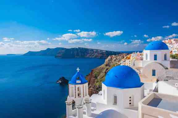 View over the ocean and santorinos iconic white buildings with blue domes roofs.