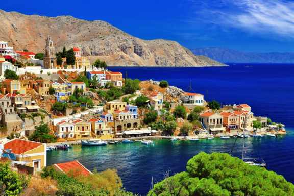 View of very colourful coastal town in the Dodecanese Islands in Greece, with mountains in the background.