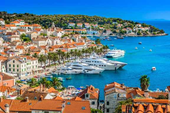 Luxury motor yachts docked in the harbour of Hvar city in Croatia surrounded by old town with red roofs.