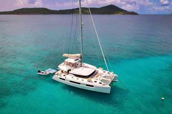 Aerial view of catamaran PURELY BLU anchored in turquoise water off the BVI with her tender and paddleboard alongside